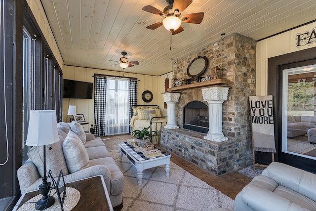 living room with a stone fireplace, wood walls, wood ceiling, and ceiling fan