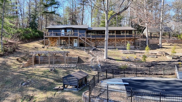 back of house with stone siding, metal roof, stairs, fence, and a pergola