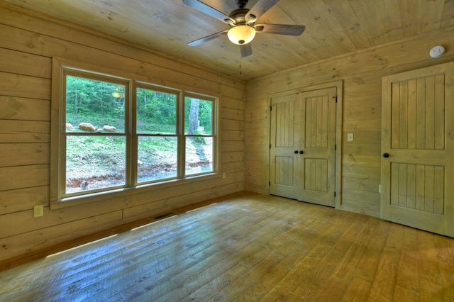 empty room with light wood finished floors, wooden walls, a ceiling fan, and visible vents