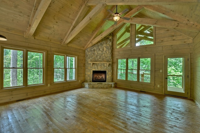 unfurnished living room featuring high vaulted ceiling, a stone fireplace, hardwood / wood-style floors, wooden walls, and beam ceiling