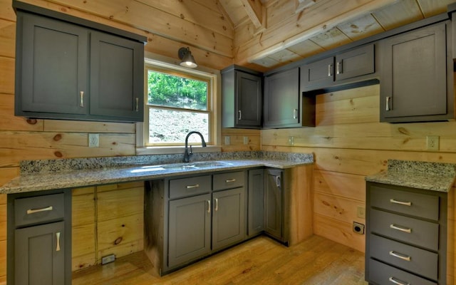 kitchen with wooden walls, light wood finished floors, a sink, and vaulted ceiling with beams