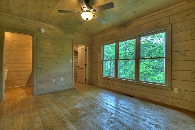 spare room with wood-type flooring, a healthy amount of sunlight, and wood walls