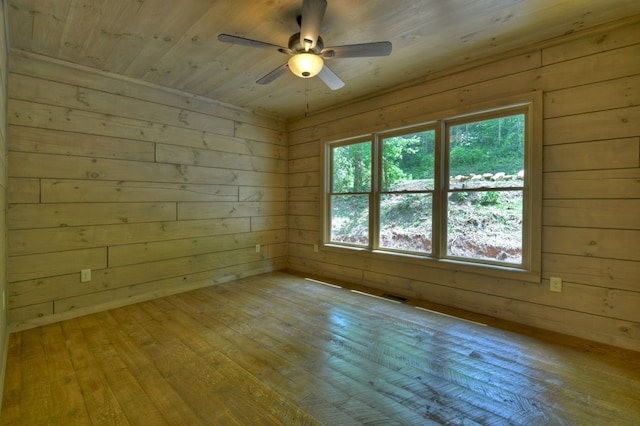 unfurnished room with wooden walls, visible vents, a ceiling fan, and hardwood / wood-style floors