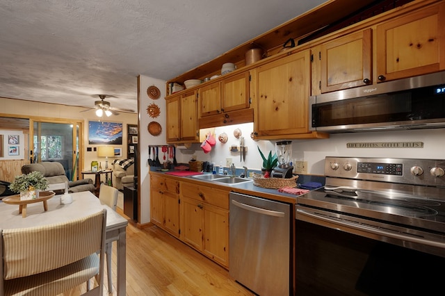 kitchen with appliances with stainless steel finishes, a textured ceiling, ceiling fan, light hardwood / wood-style flooring, and sink