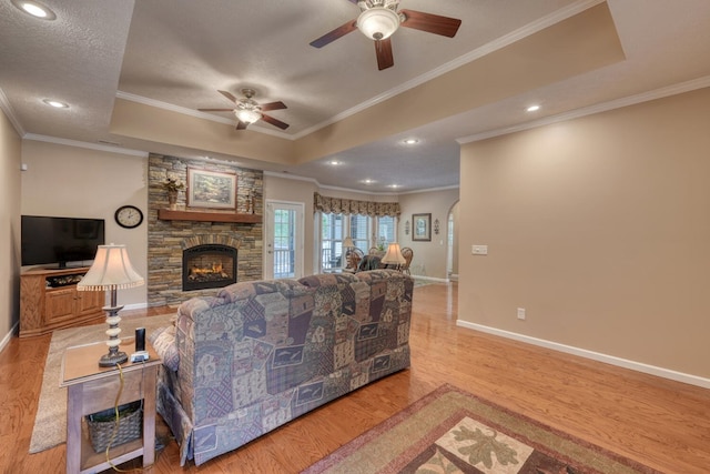 living area with a ceiling fan, crown molding, a fireplace, wood finished floors, and a raised ceiling