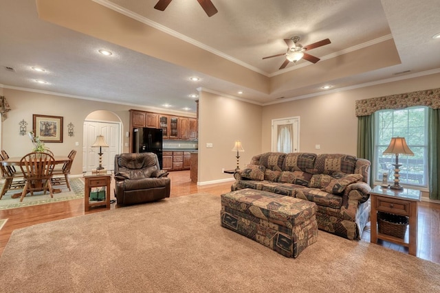 living room with crown molding, arched walkways, a ceiling fan, and a raised ceiling