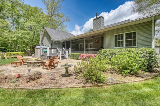 rear view of property with ceiling fan, a fire pit, a deck, a patio, and a chimney