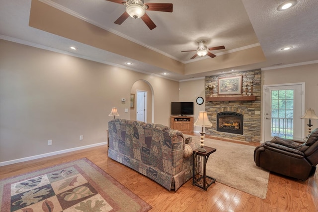 living area featuring crown molding, light wood finished floors, arched walkways, a ceiling fan, and a tray ceiling