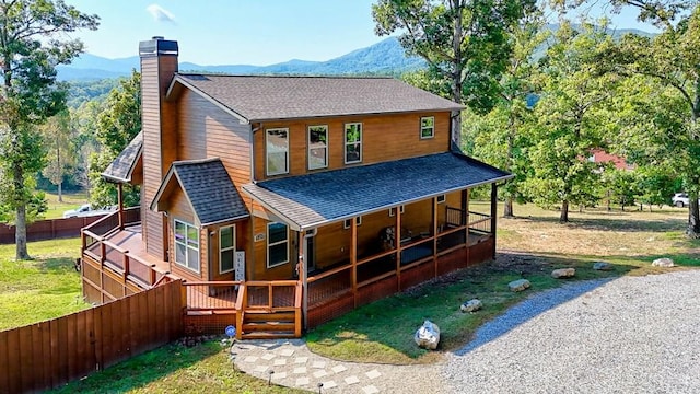 back of house with driveway, a shingled roof, a chimney, fence, and a mountain view