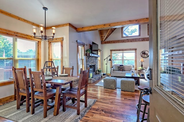 dining room featuring vaulted ceiling with beams, an inviting chandelier, a stone fireplace, wood finished floors, and baseboards