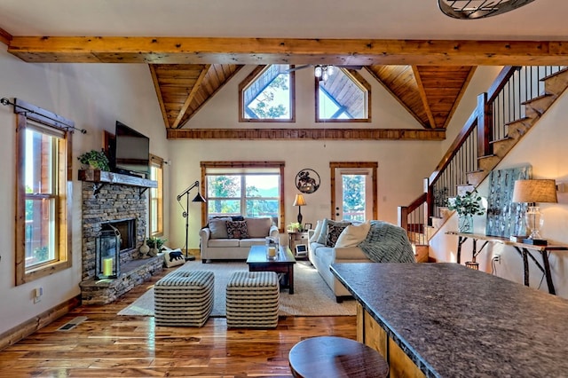 living area featuring beam ceiling, visible vents, a stone fireplace, wood finished floors, and stairs