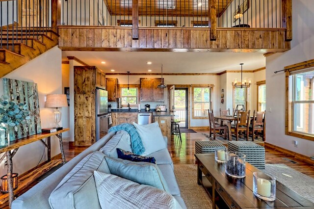 living area featuring a towering ceiling, baseboards, wood finished floors, and ornamental molding