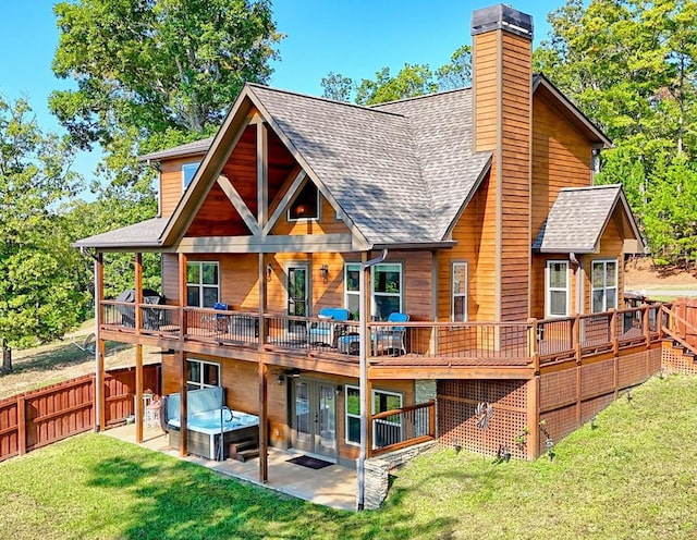 rear view of house with a shingled roof, a patio area, a yard, and a hot tub