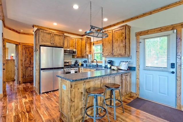 kitchen with dark countertops, appliances with stainless steel finishes, brown cabinetry, a sink, and a peninsula