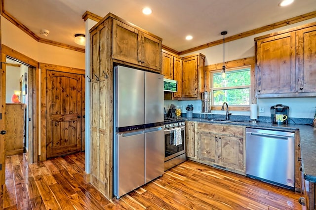 kitchen featuring stainless steel appliances, wood finished floors, dark countertops, and a sink