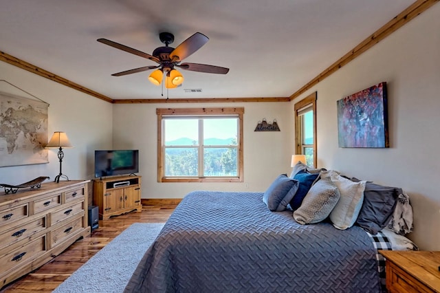 bedroom featuring ceiling fan, wood finished floors, visible vents, and crown molding