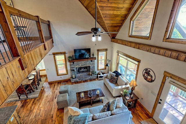 living room with high vaulted ceiling, a stone fireplace, wood finished floors, and a healthy amount of sunlight