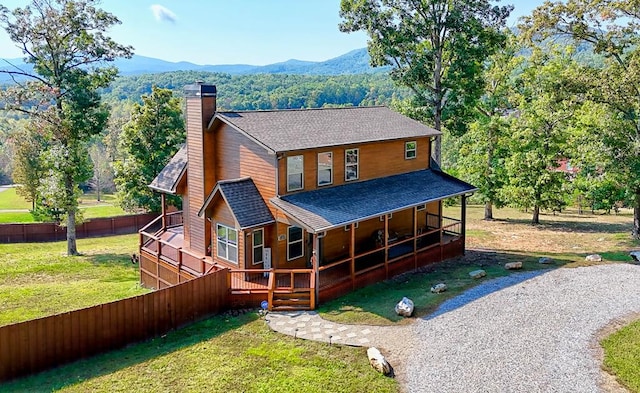 rear view of house featuring roof with shingles, a yard, a chimney, a mountain view, and driveway