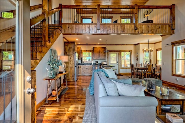 living area with a chandelier, a towering ceiling, baseboards, stairs, and dark wood finished floors