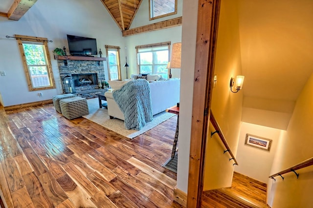 living area featuring baseboards, wood finished floors, a stone fireplace, high vaulted ceiling, and beam ceiling