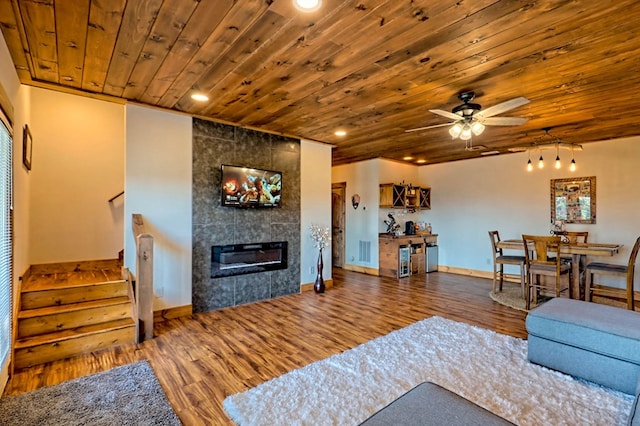 living area featuring stairs, a tile fireplace, wood ceiling, and wood finished floors