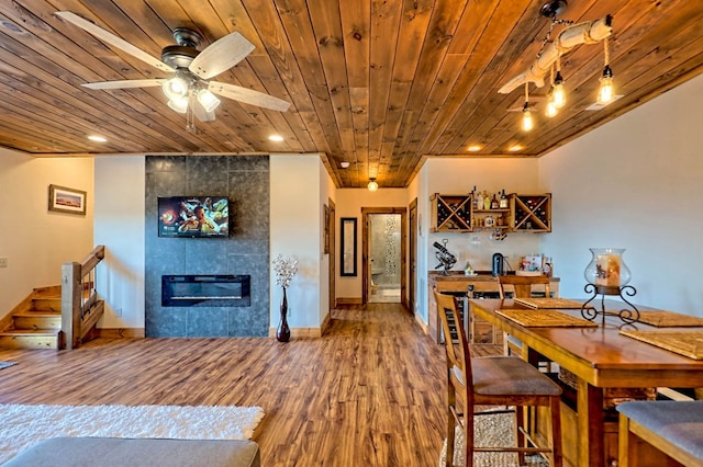 dining room featuring a tile fireplace, wood finished floors, wood ceiling, and a ceiling fan