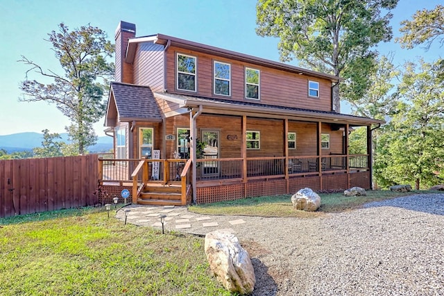 view of front of property with a shingled roof, a chimney, a porch, fence, and a front lawn