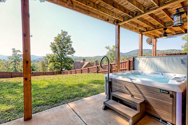 view of patio featuring fence, a mountain view, and a hot tub