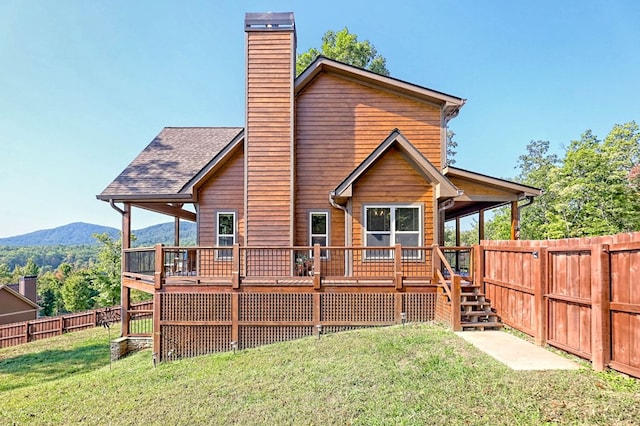 rear view of property with a deck with mountain view, a fenced backyard, a yard, roof with shingles, and a chimney