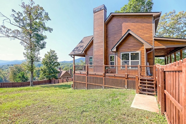 rear view of property featuring a deck with mountain view, a fenced backyard, a chimney, and a lawn