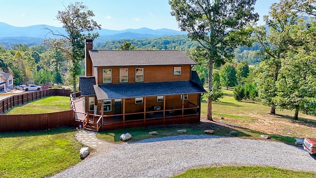 back of property with covered porch, a chimney, a mountain view, and a lawn