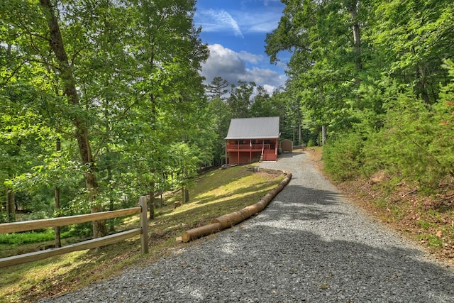 chalet / cabin with gravel driveway, a forest view, and fence