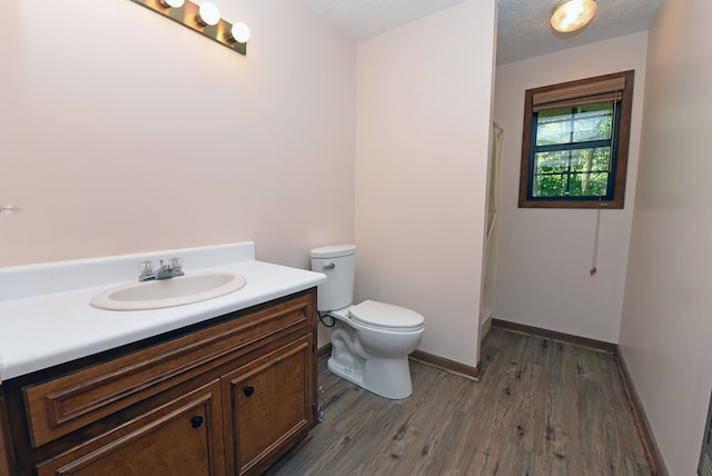 bathroom with a textured ceiling, wood-type flooring, vanity, and toilet