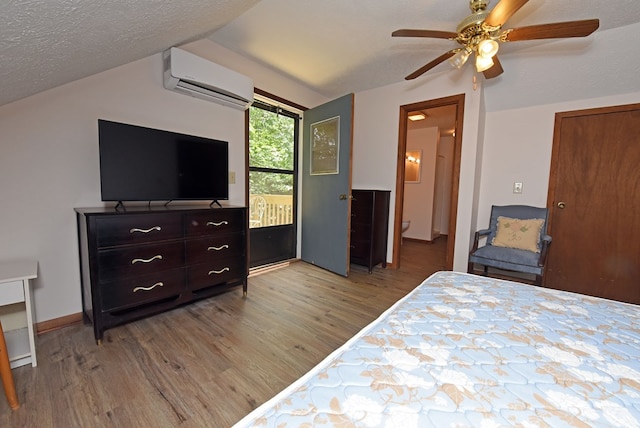 bedroom featuring light hardwood / wood-style floors, a textured ceiling, a wall unit AC, ensuite bath, and ceiling fan