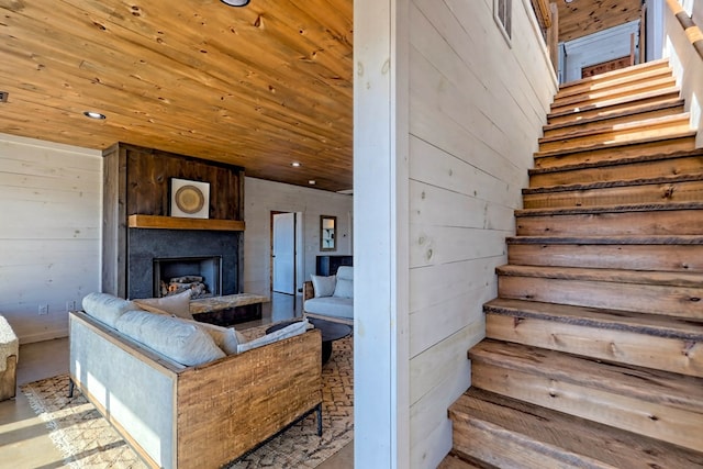 staircase featuring wood ceiling, wooden walls, a fireplace with raised hearth, and recessed lighting