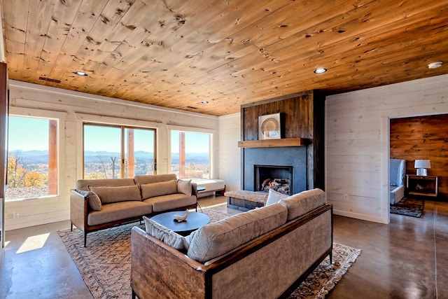 living area featuring finished concrete flooring, a mountain view, a fireplace with raised hearth, wooden ceiling, and wooden walls