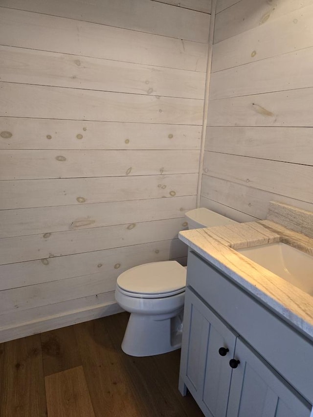 bathroom with vanity, hardwood / wood-style floors, wooden walls, and toilet