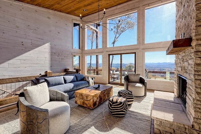 living area with a towering ceiling, a notable chandelier, a mountain view, a stone fireplace, and wooden ceiling