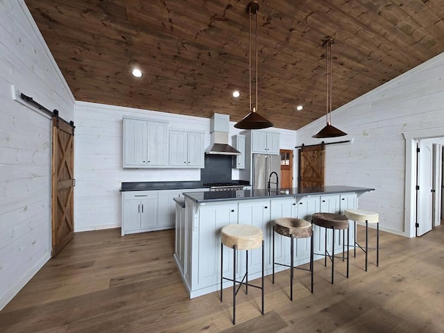 kitchen featuring white cabinetry, light hardwood / wood-style floors, wall chimney exhaust hood, and a barn door