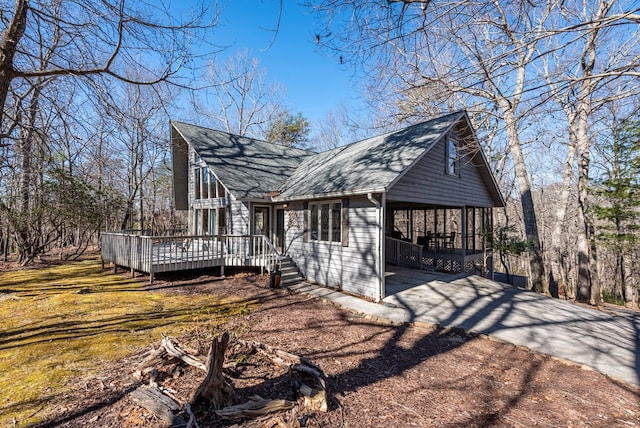 view of side of property featuring a carport, a deck, concrete driveway, and roof with shingles