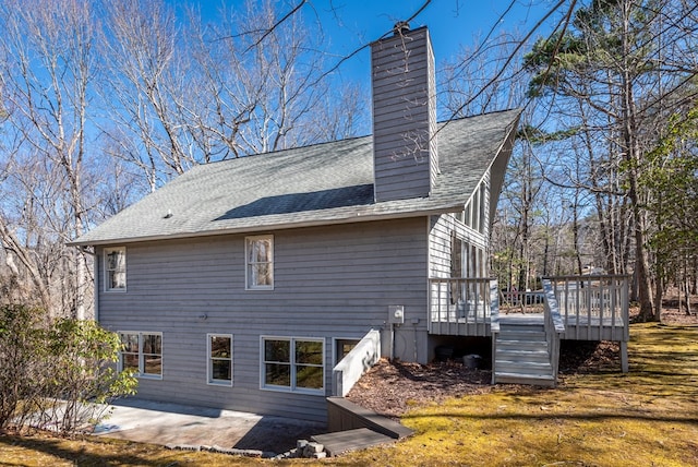 rear view of property with roof with shingles, a chimney, a deck, and a patio