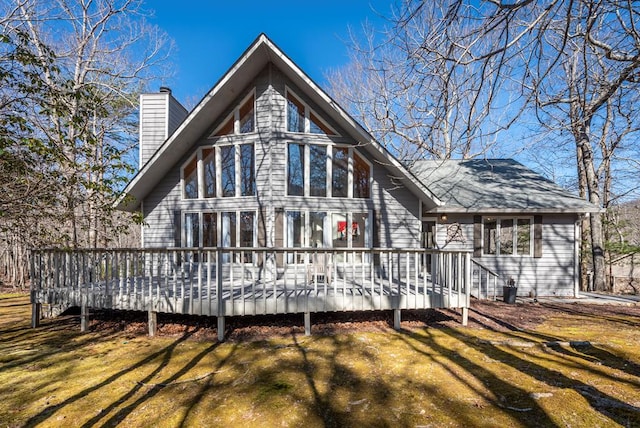 rear view of property featuring a chimney, a deck, and a yard