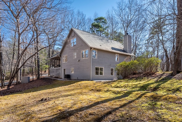 view of side of property featuring a sunroom, a chimney, central AC, and a yard