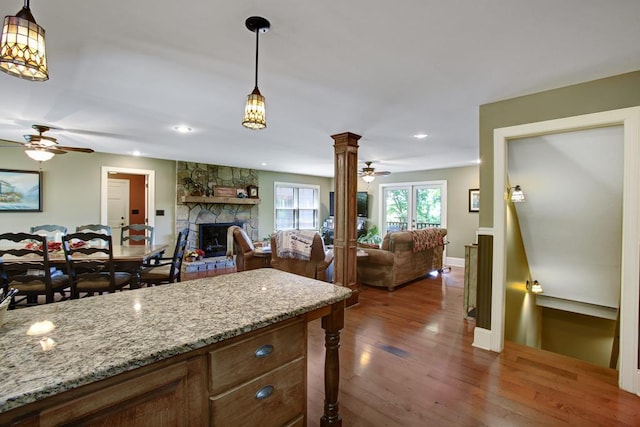 kitchen featuring a stone fireplace, hanging light fixtures, dark hardwood / wood-style flooring, light stone counters, and decorative columns