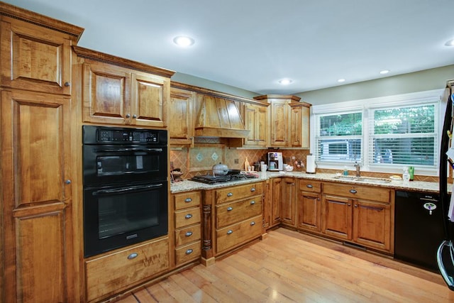 kitchen with sink, light stone counters, light hardwood / wood-style flooring, black appliances, and custom range hood