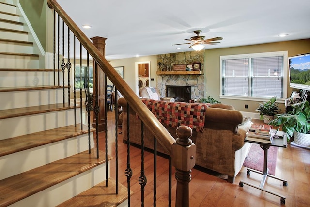 living room featuring hardwood / wood-style flooring, ceiling fan, and a stone fireplace