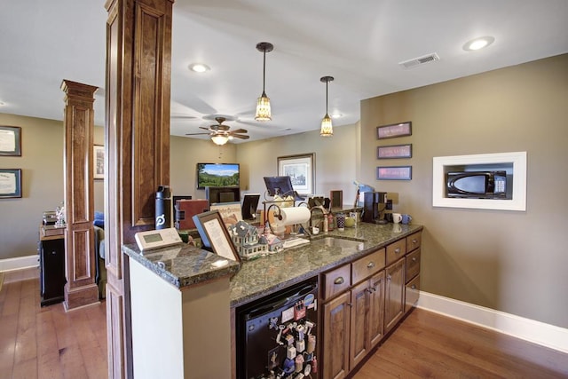 kitchen with ornate columns, dishwasher, dark hardwood / wood-style floors, kitchen peninsula, and dark stone countertops