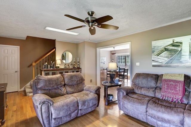 living room with light wood-type flooring, crown molding, ceiling fan, and a textured ceiling