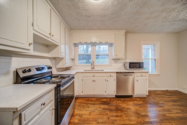 kitchen featuring stainless steel appliances, a sink, light countertops, decorative backsplash, and dark wood-style floors