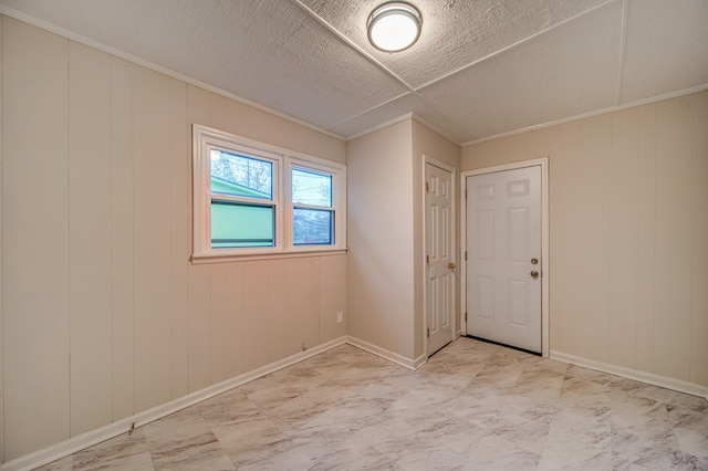 empty room featuring ornamental molding, marble finish floor, a textured ceiling, and baseboards